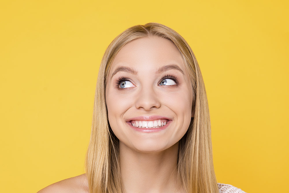 Portrait of cheerful toothy girl with naked shoulder looking with eyes at copyspace empty place having white straight healthy teeth isolated on yellow background